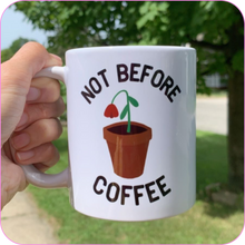 Load image into Gallery viewer, Rhonda&#39;s hand holding the Not Before Coffee Mug on a bright, sunny day, with grass and a tree in the background